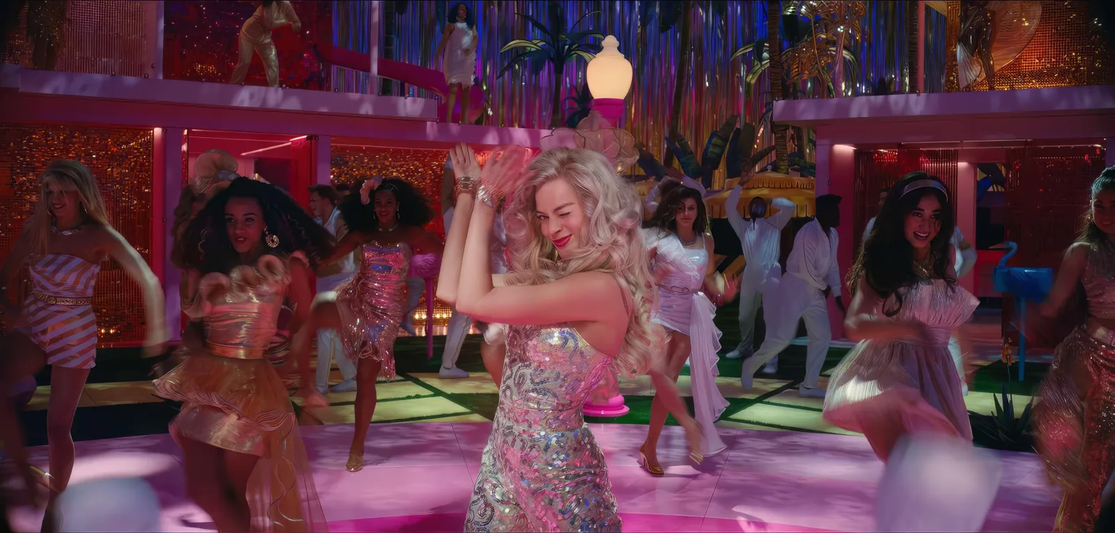 A dancer mid-turn on a bright pink dance floor, a full company of dancers moving behind her under disco lighting