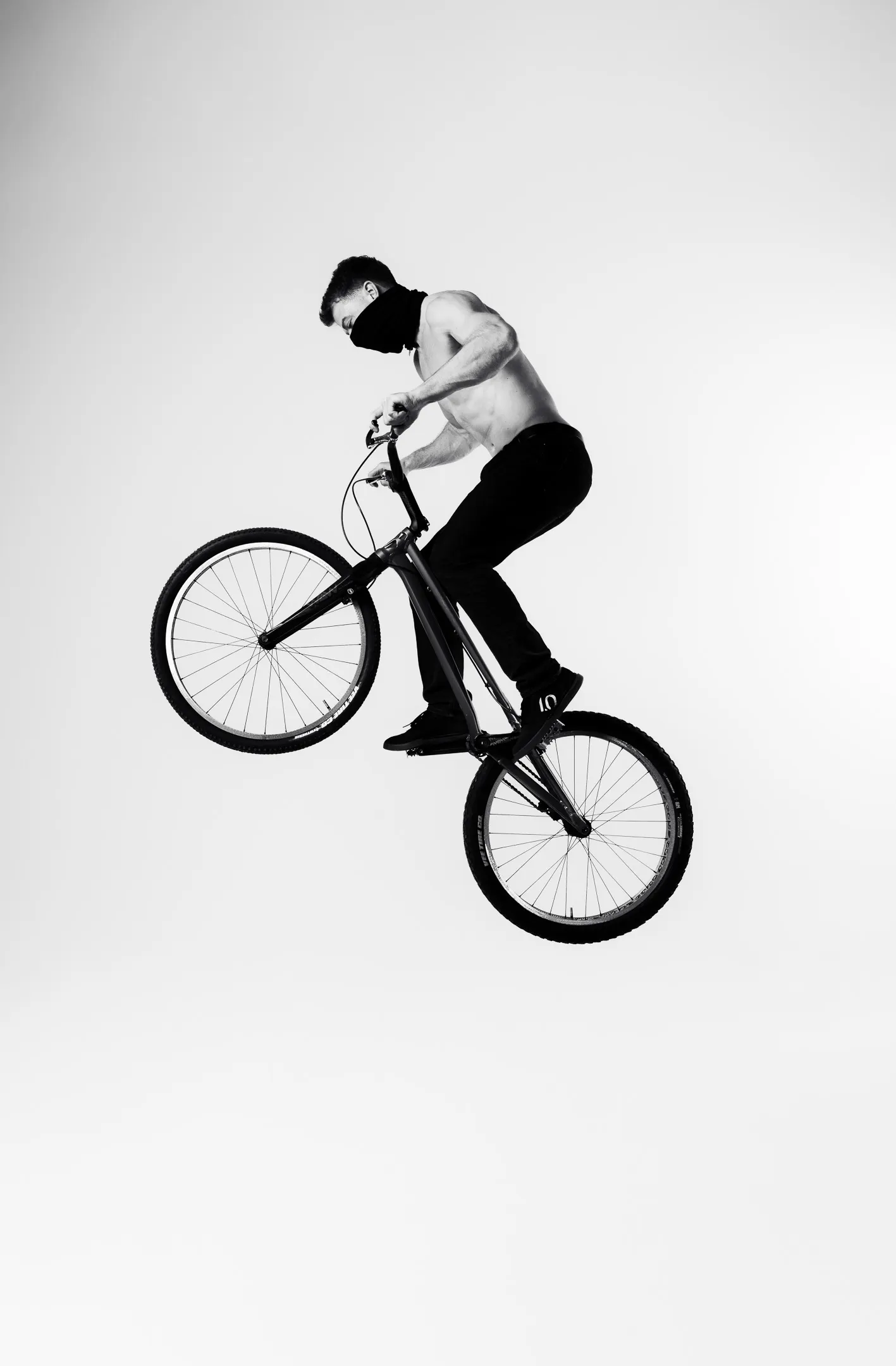 A trials rider mid-air on a bike, photographed in black and white against a plain studio backdrop.