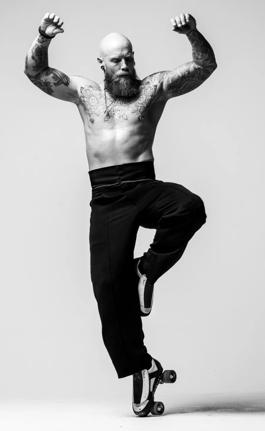 A tattooed roller skater facing the camera on one skate, arms flexed.