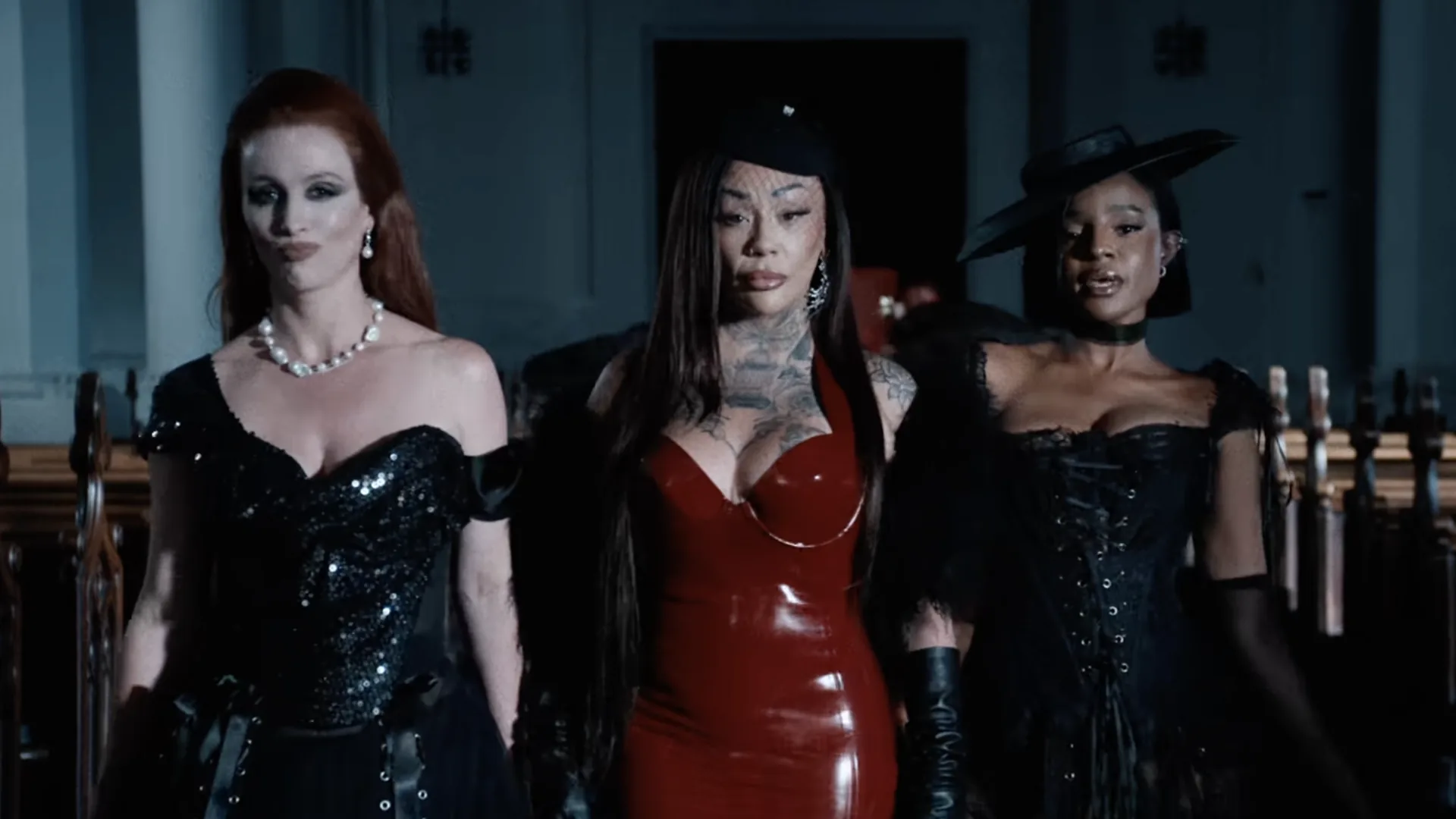 Three performers in black and red walking between church pews in the Sugababes’ Ghost video