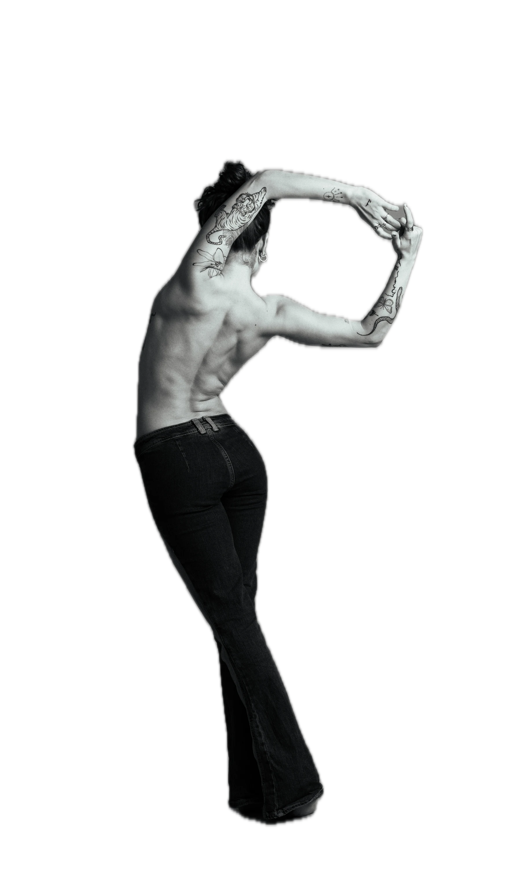 A performer seen from behind, arms raised and hands clasped above her head, photographed in a studio.