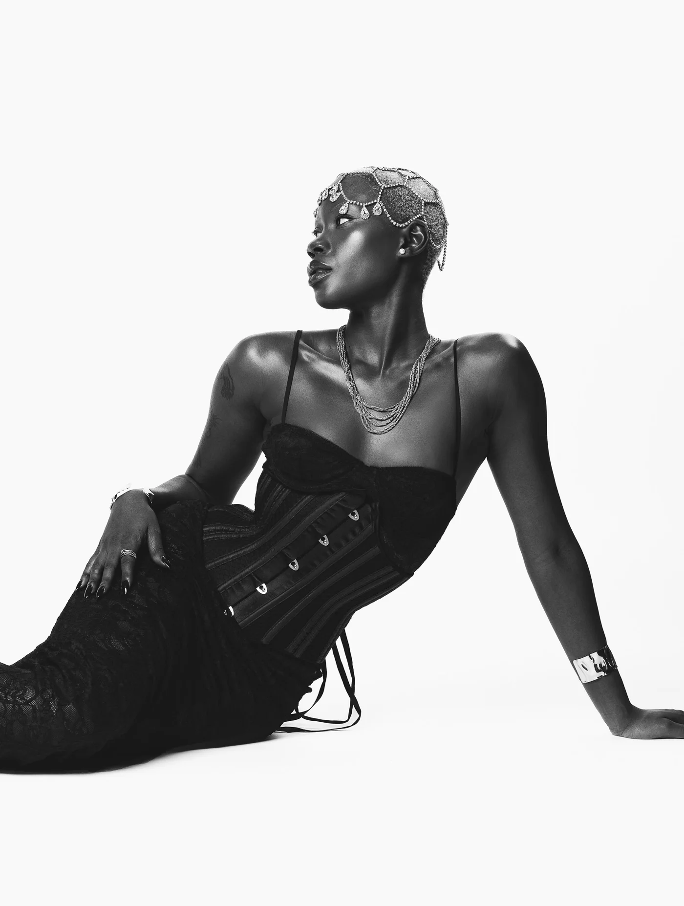 Black and white campaign still of a model reclining in a laced corset and lace skirt against a white background