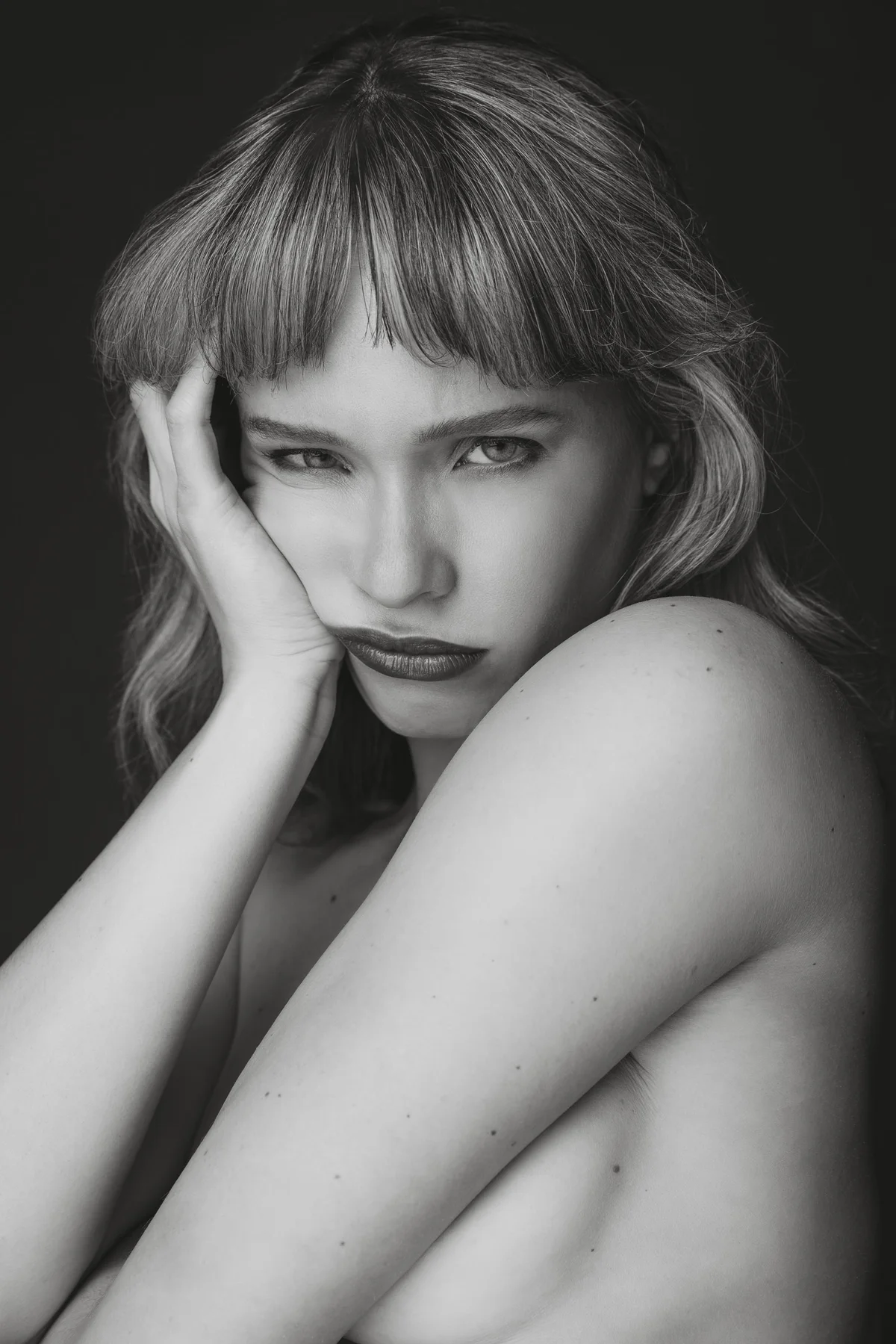 Black and white portrait of a model resting her cheek on her hand, looking straight to camera