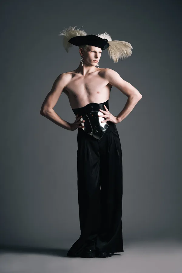 Model in a plumed tricorn hat and mirrored corset, hands on hips