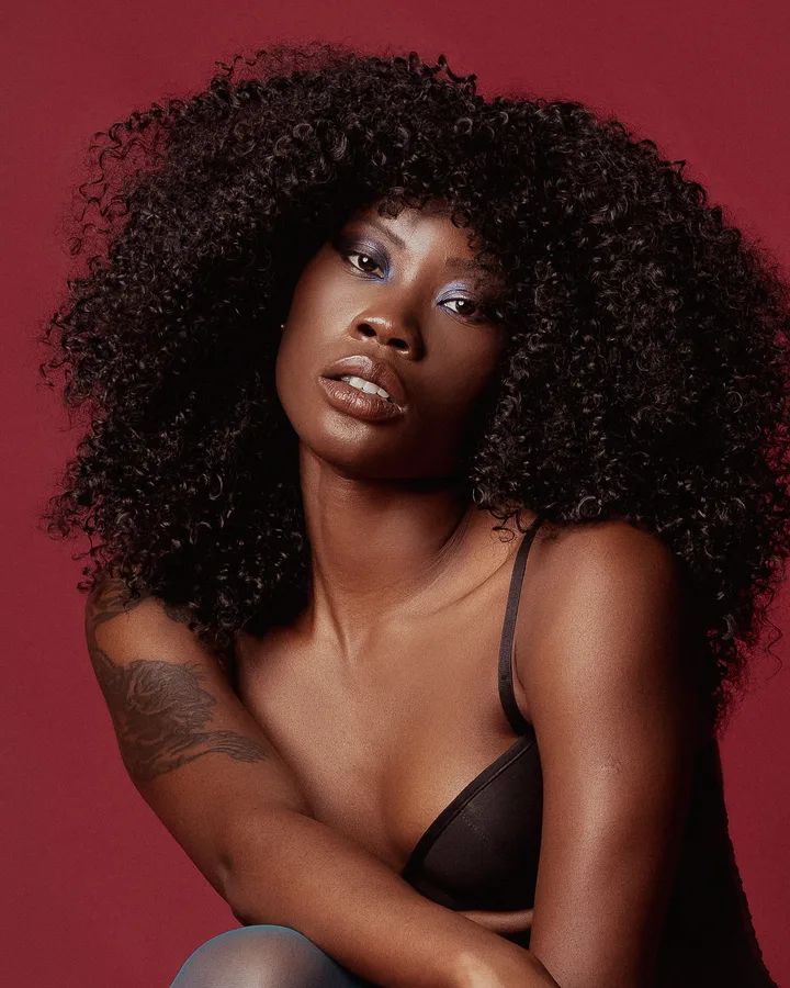 Model with a full afro and blue eyeshadow against a crimson backdrop