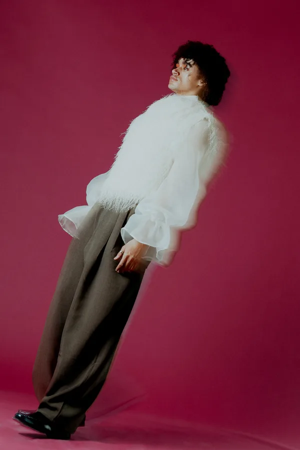 Model in a white fringed vest leaning back against a pink backdrop, motion-blurred