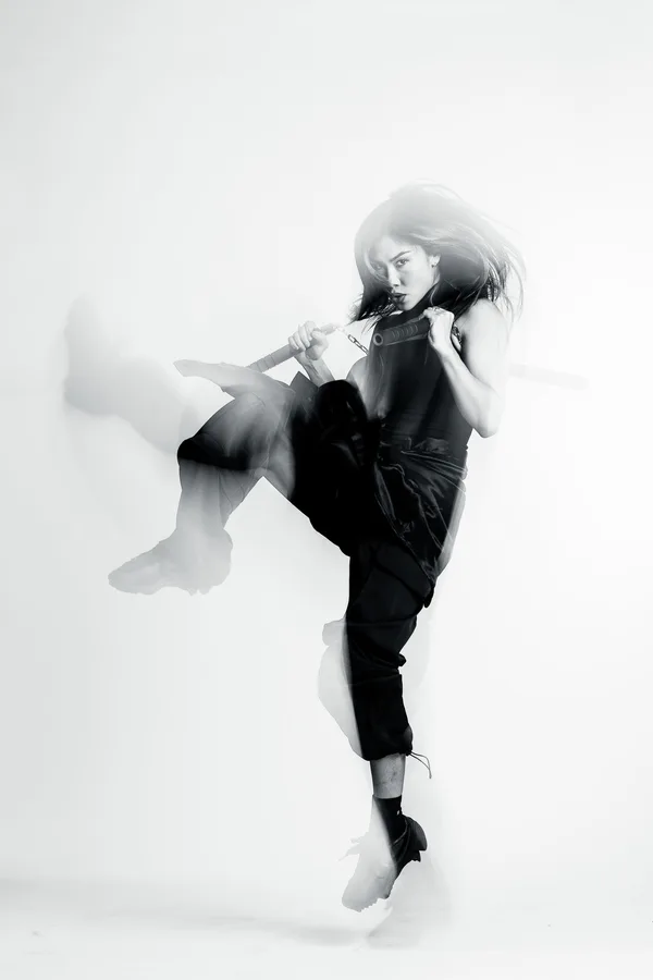 Black and white shot of a model mid-kick holding nunchucks, motion-blurred
