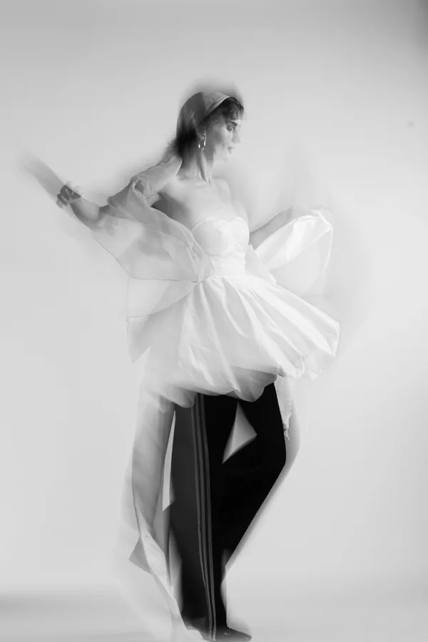 Black and white shot of a model in a white strapless dress and track trousers, mid-turn