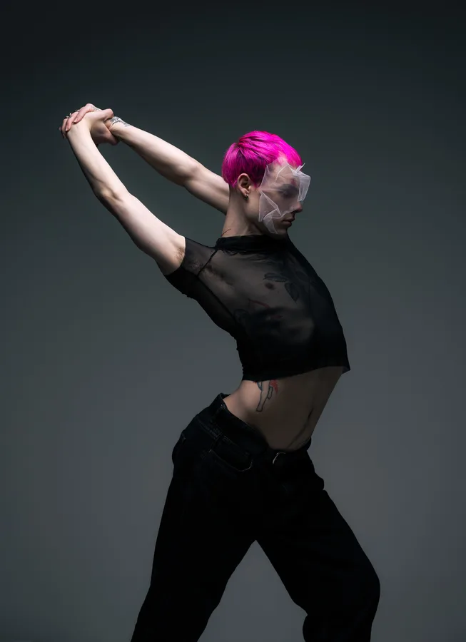 Model with pink hair in a sheer crop top, arms stretched out behind him