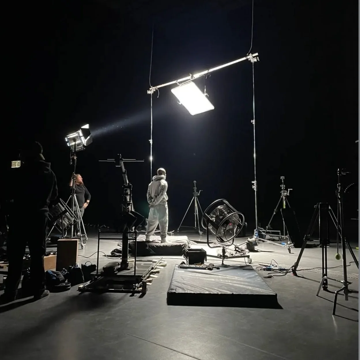 A stand-in holds a mark on a darkened stage while the crew set a large overhead soft light around them