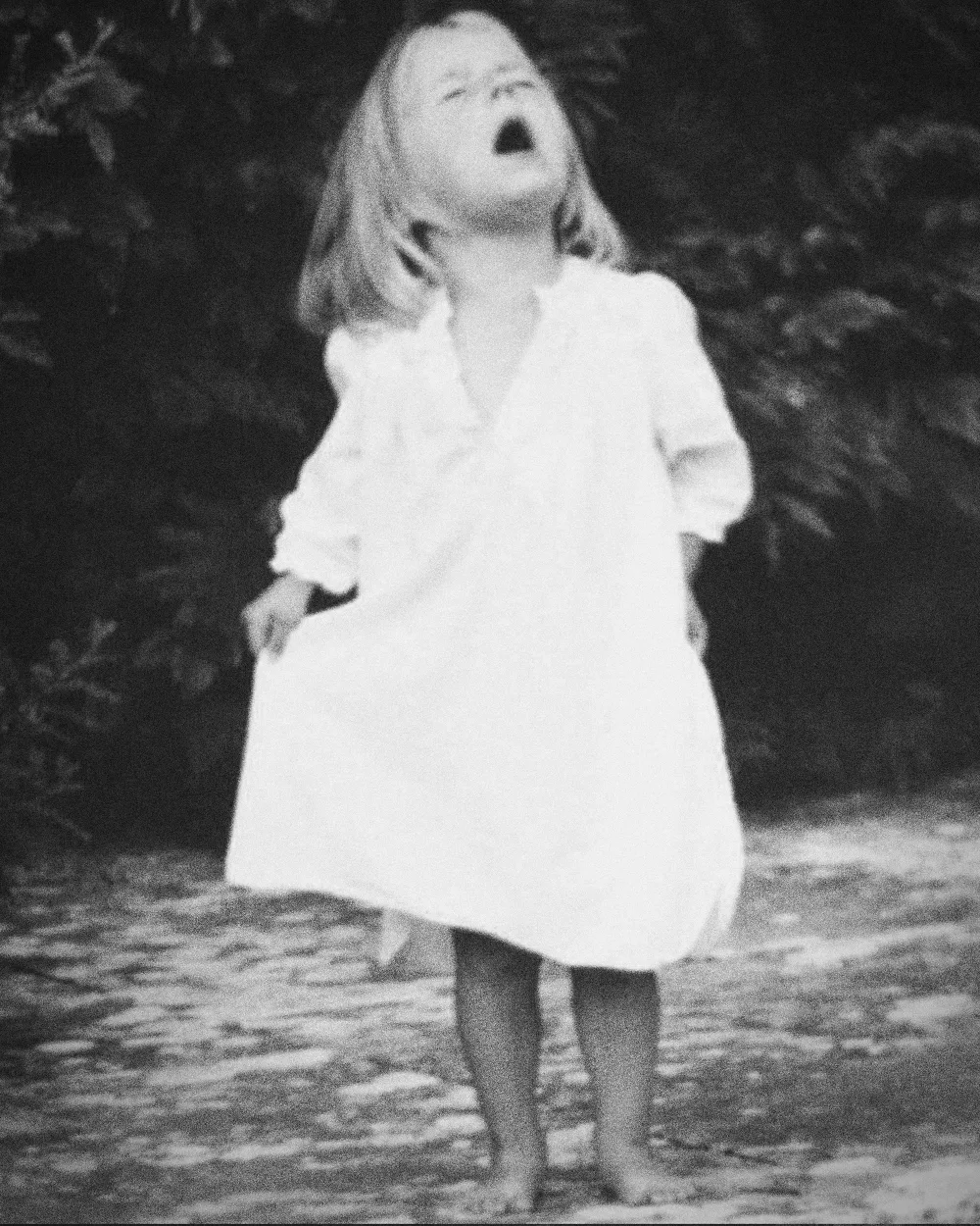 Mia as a young girl in a white nightdress, barefoot in a garden, head thrown back mid-song