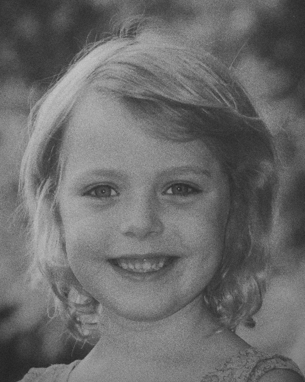 Zoë as a young girl, smiling broadly in a floral dress with trees behind her